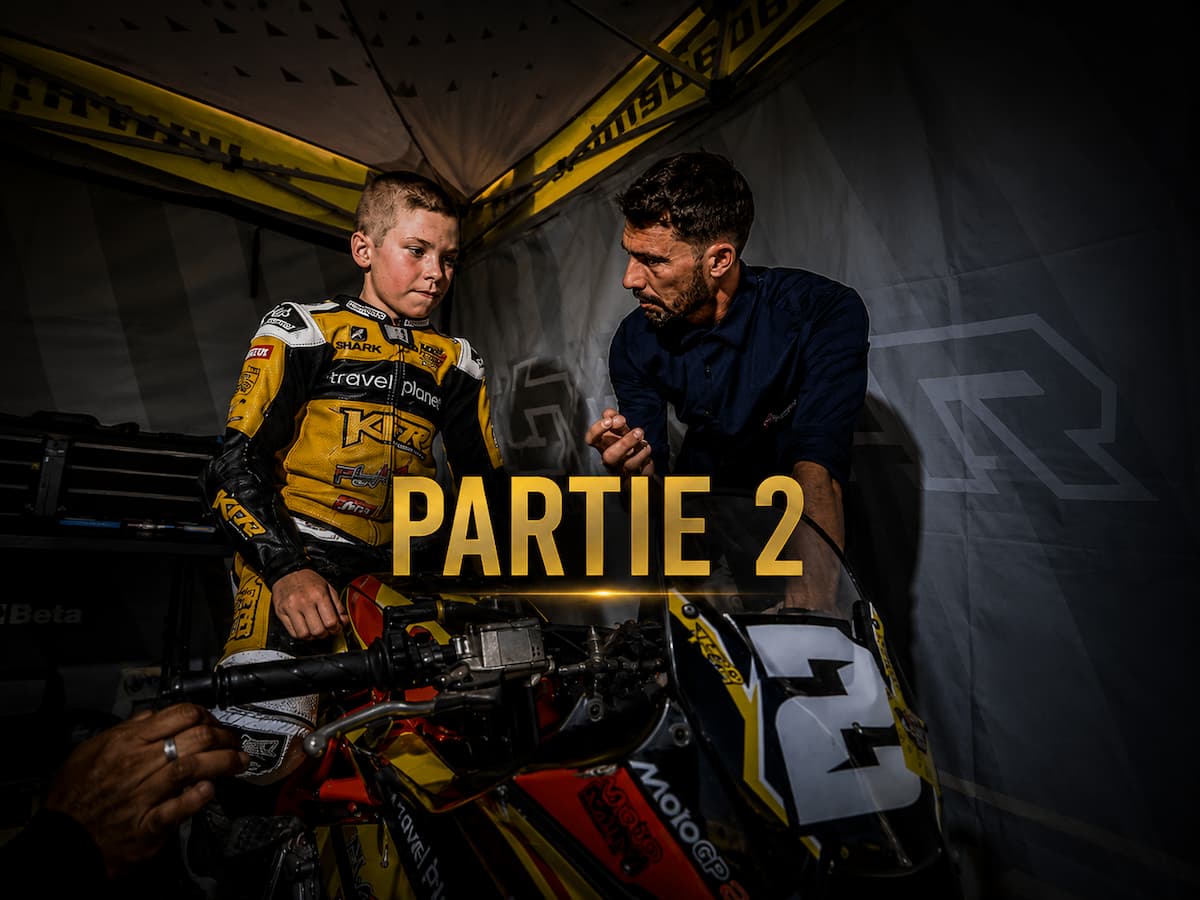 Casque de pilote posé sur une moto, virage de circuit en arrière-plan, lumière rasante
